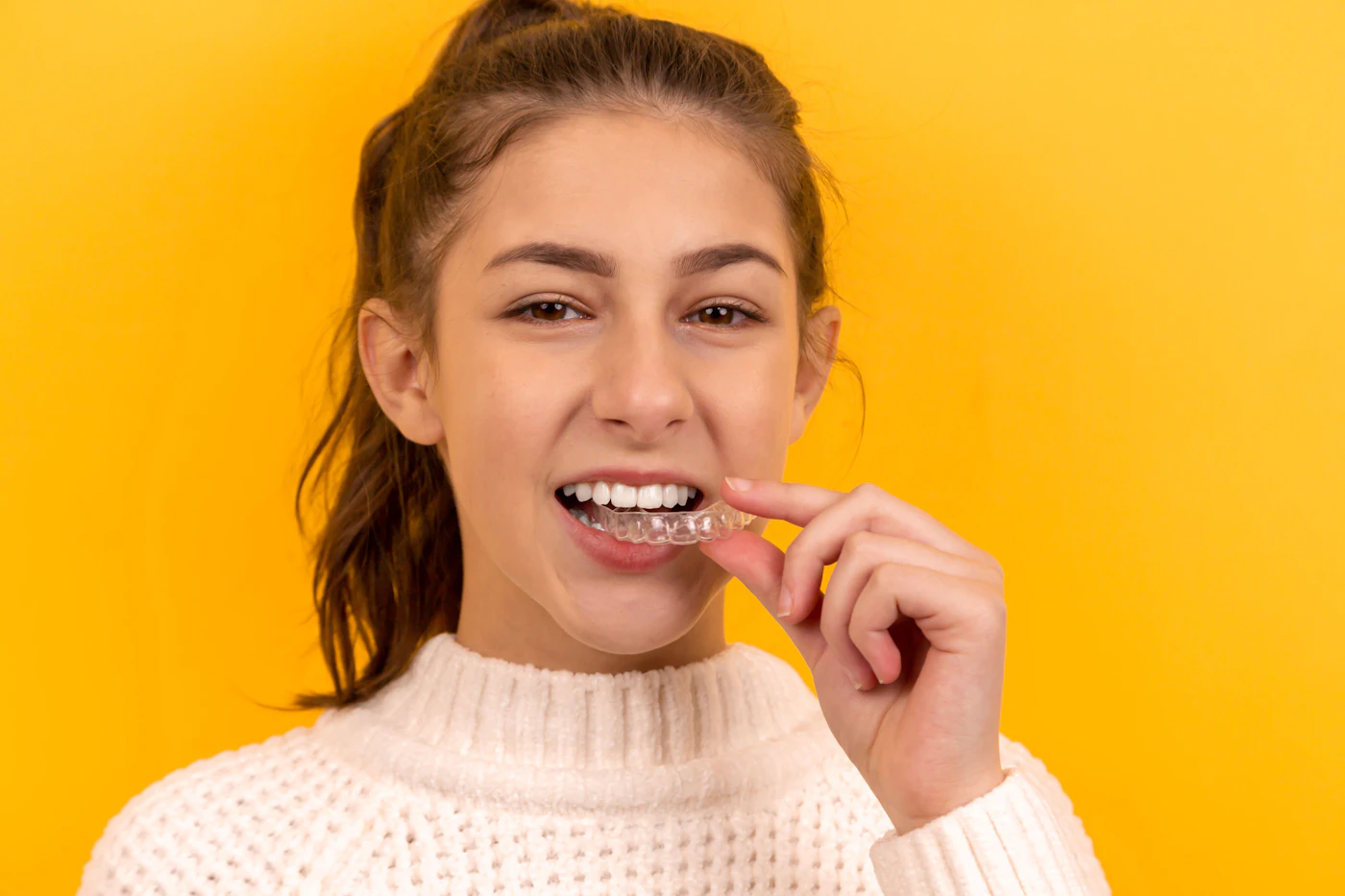 A smiling young woman fitting a clear aligner
