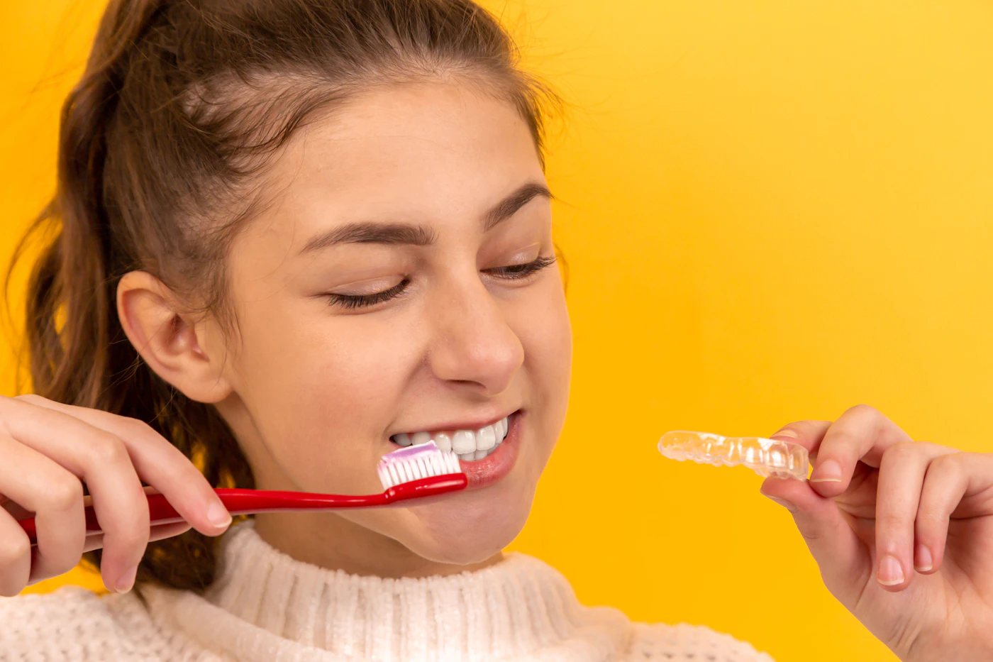 A girl smiling while holding her clear retainer